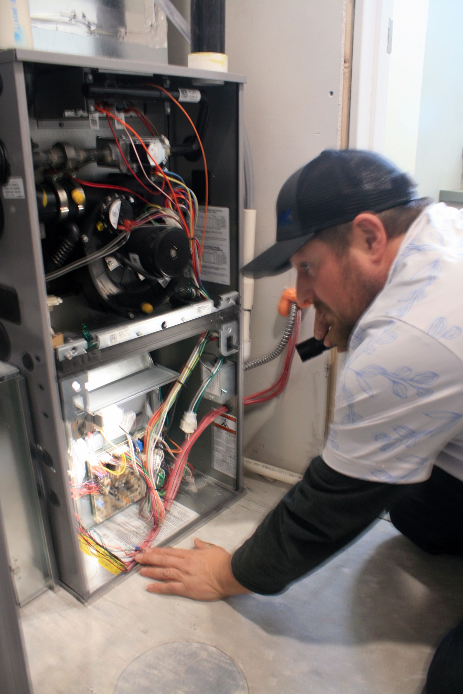 Technician kneels beside an open electrical panel, inspecting wiring in a utility room.