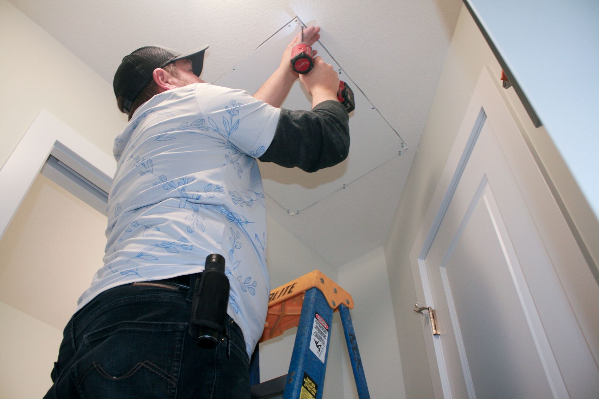 A man is standing on a ladder working on a ceiling.
