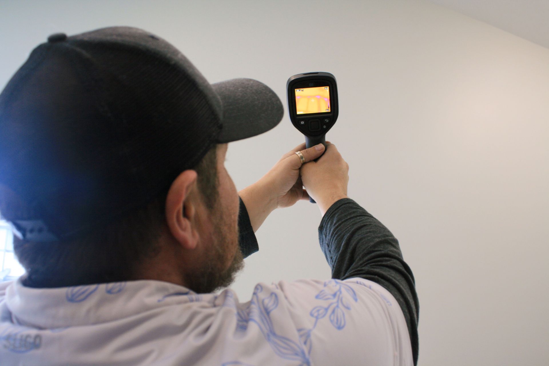 A person wearing a tool belt and dark clothing climbs a ladder against the white siding of a house with a brick chimney.