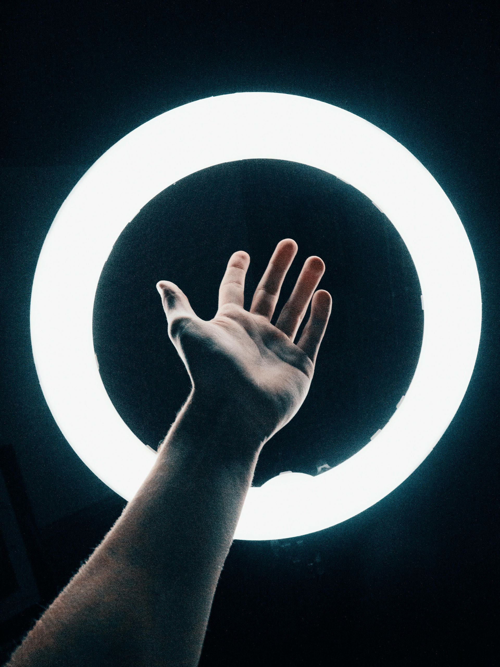 Hand reaching out in front of a ring light against black background