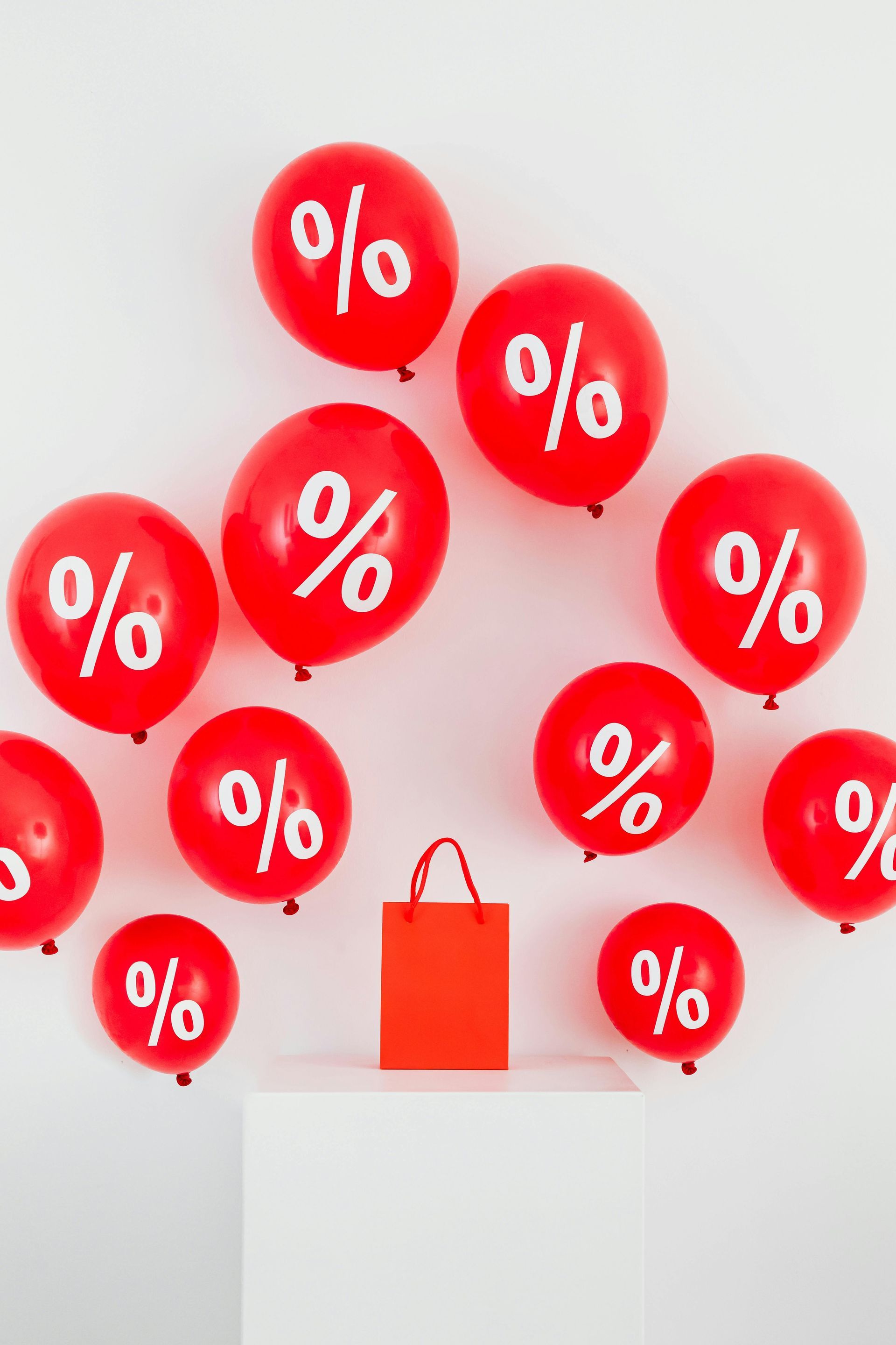 Red balloons with the percent sign on them surrounding a red bag