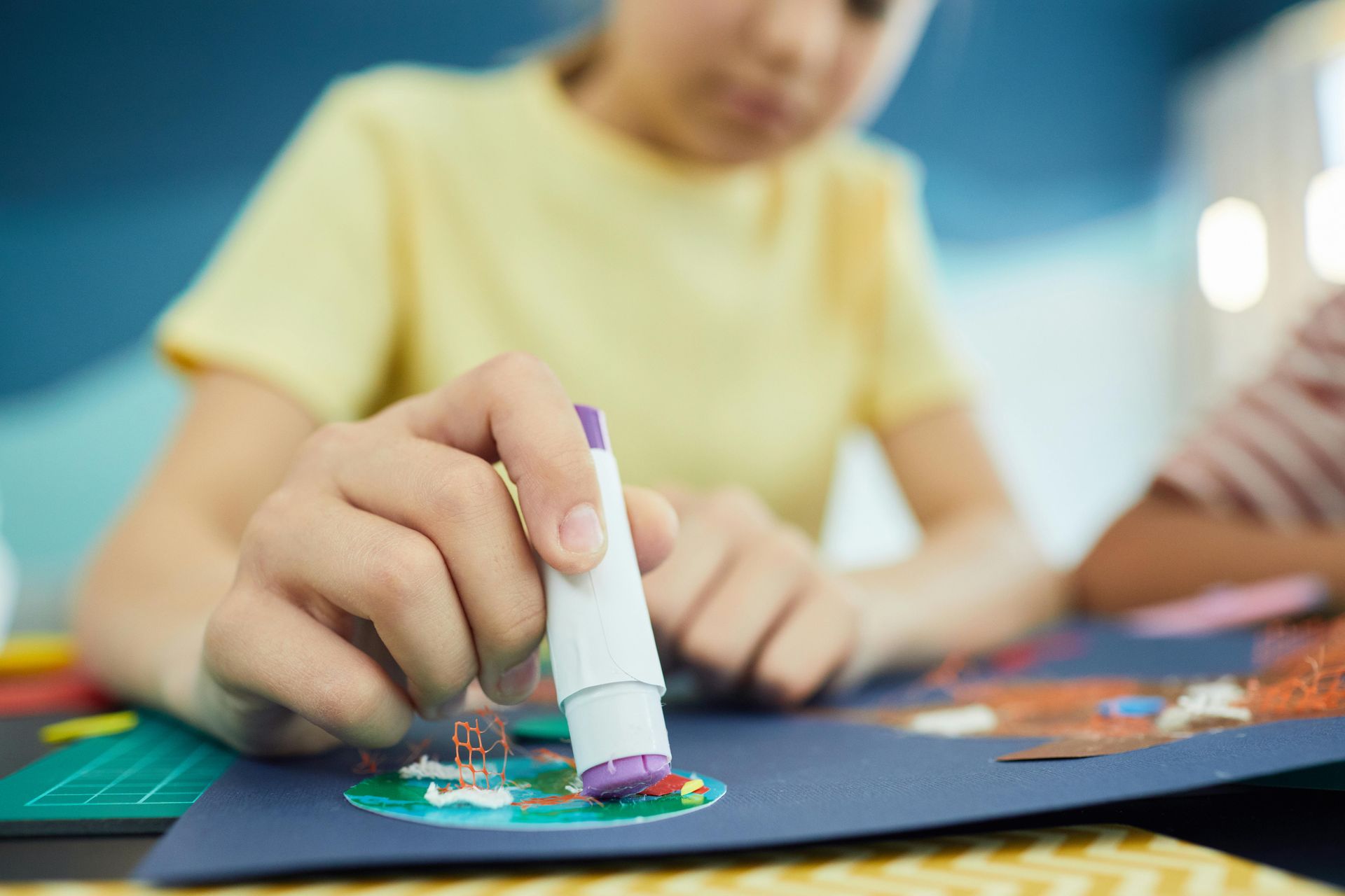 Young girl with a glue stick over construction paper