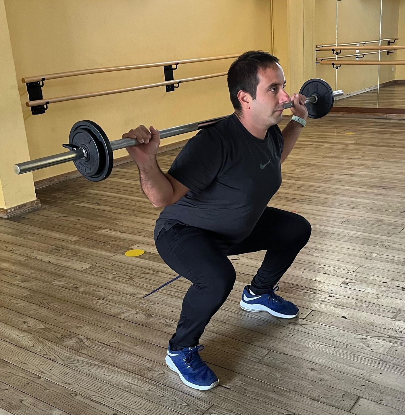 Una persona in palestra esegue uno squat con bilanciere, indossando abbigliamento sportivo, posizionata di fronte a una parete a specchio.