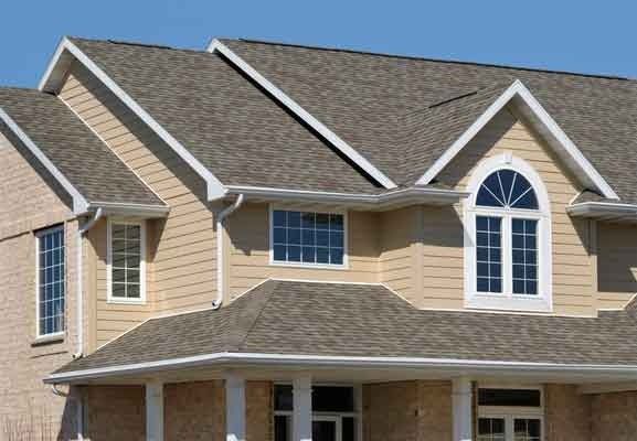 Beige suburban house with a gray shingled roof and white-trimmed arched windows