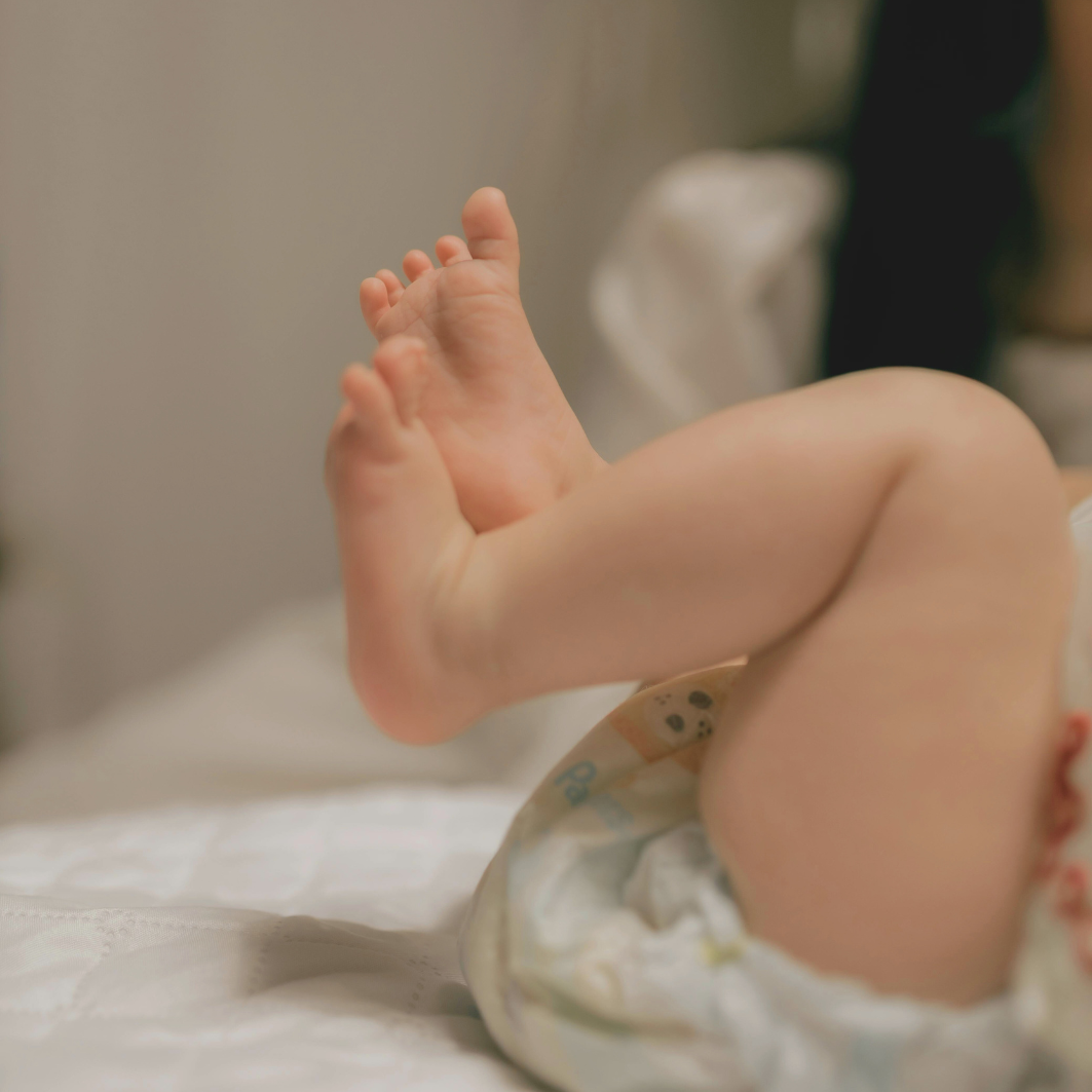 A close-up view of a baby's feet and legs, resting in a diaper on a white surface.