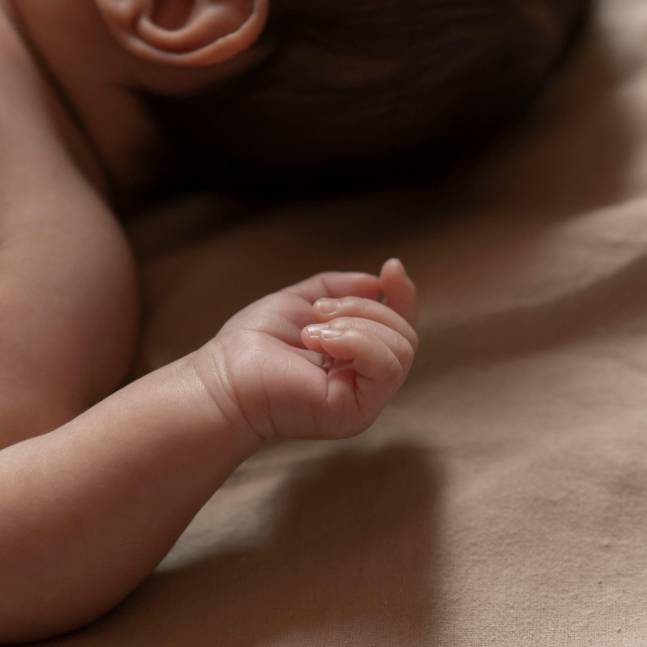 A close-up of a small, soft hand resting on a smooth, tan surface near the back of a head.