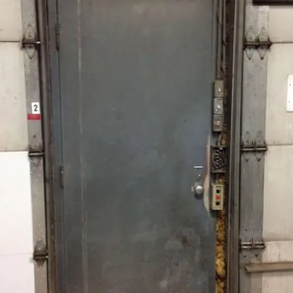 Metal door, gray, with control panel and red button, mounted in concrete wall.