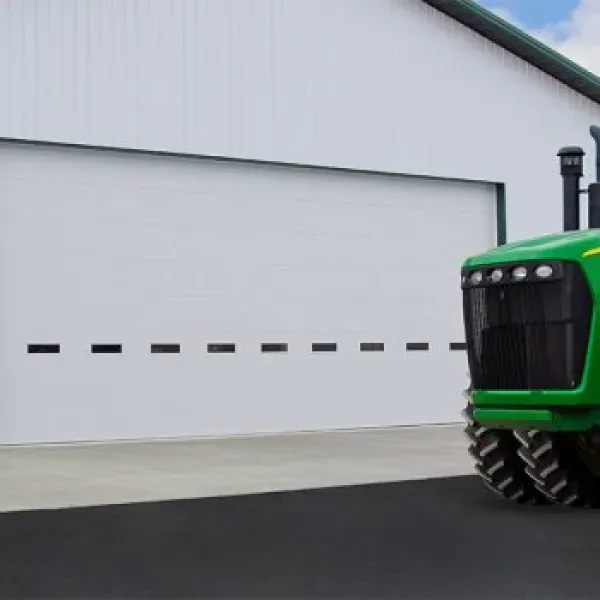 Green tractor in front of a white agricultural building with a large closed door.