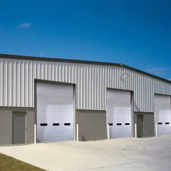 A white industrial building with three garage doors and a concrete apron. Blue sky in background.