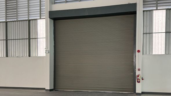 Warehouse with a closed, brown rolling shutter door; windows on either side and above.