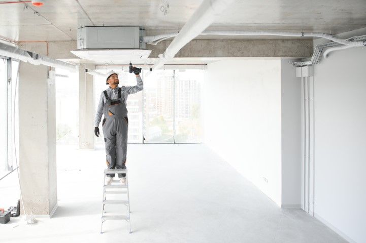 A man is standing on a ladder fixing a ceiling fan.