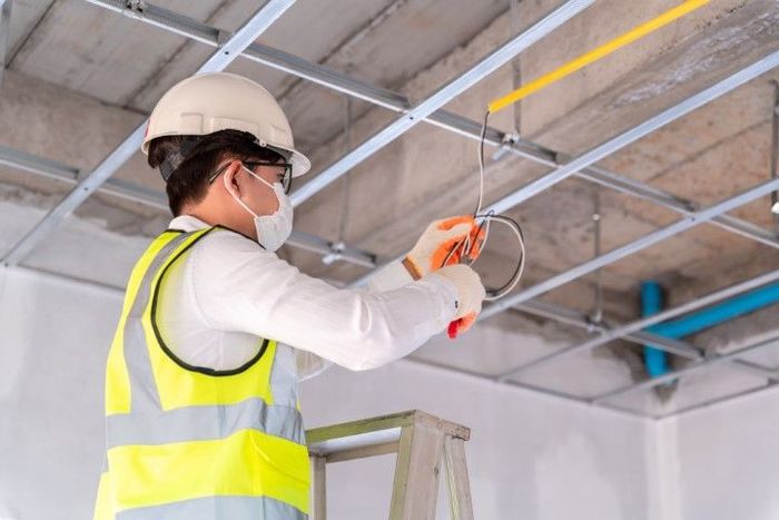 A man wearing a hard hat and safety vest is working on a ceiling.
