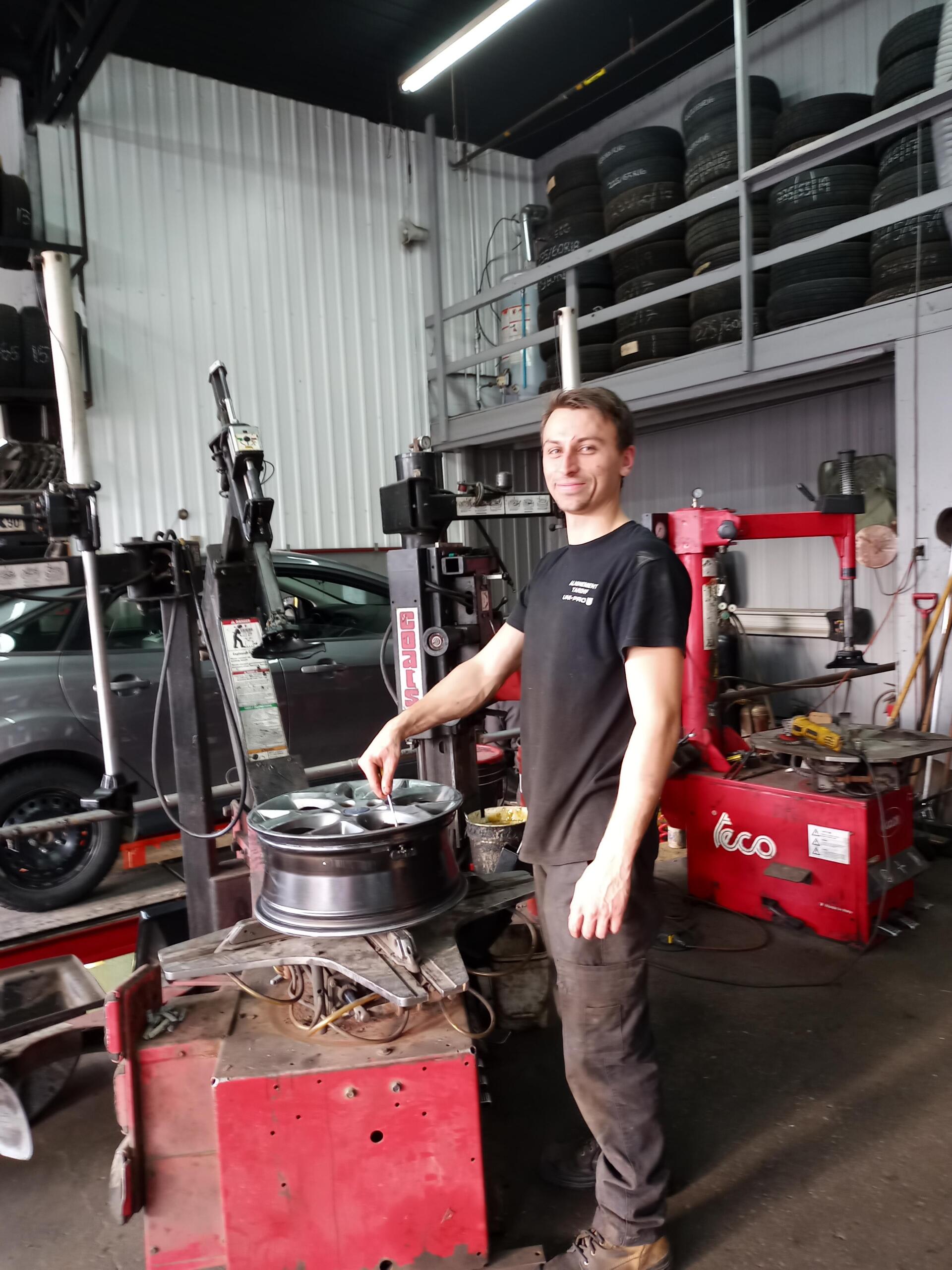 Un homme se tient devant une machine à pneus dans un garage.