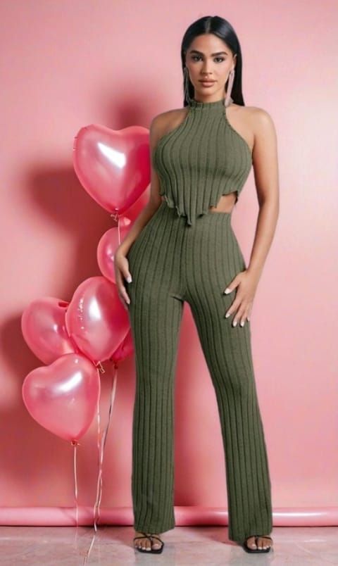 Una mujer con un conjunto de punto acanalado verde oliva posa junto a globos con forma de corazón sobre un fondo rosa.
