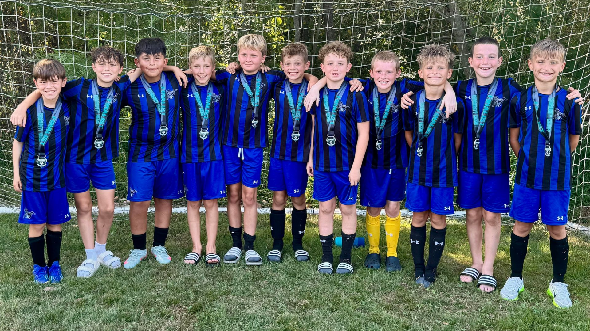 Youth soccer team in blue and black striped jerseys poses for a team photo on a green field.