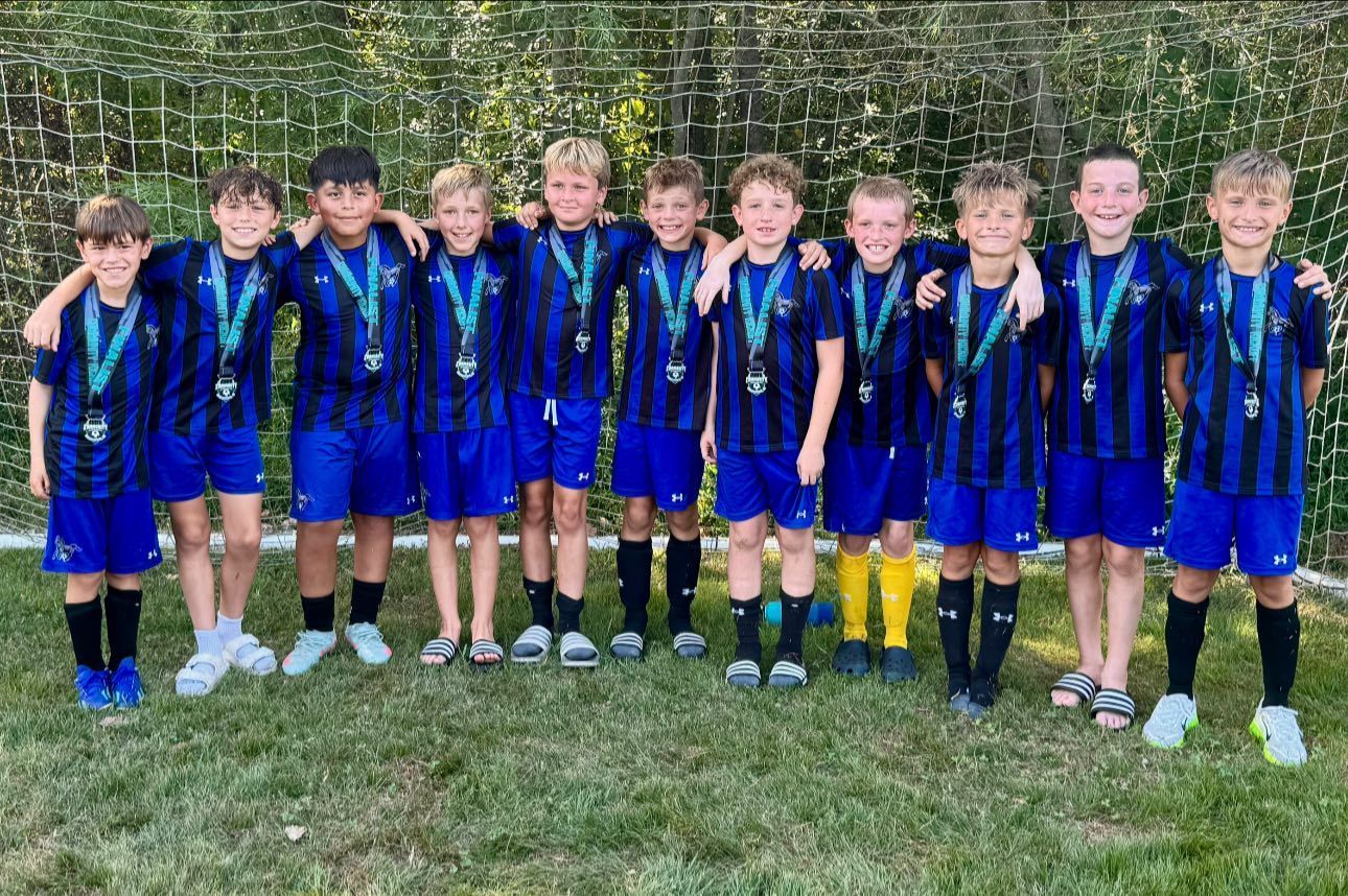 Youth soccer team in blue uniforms, posing on the field after a game, wearing medals.