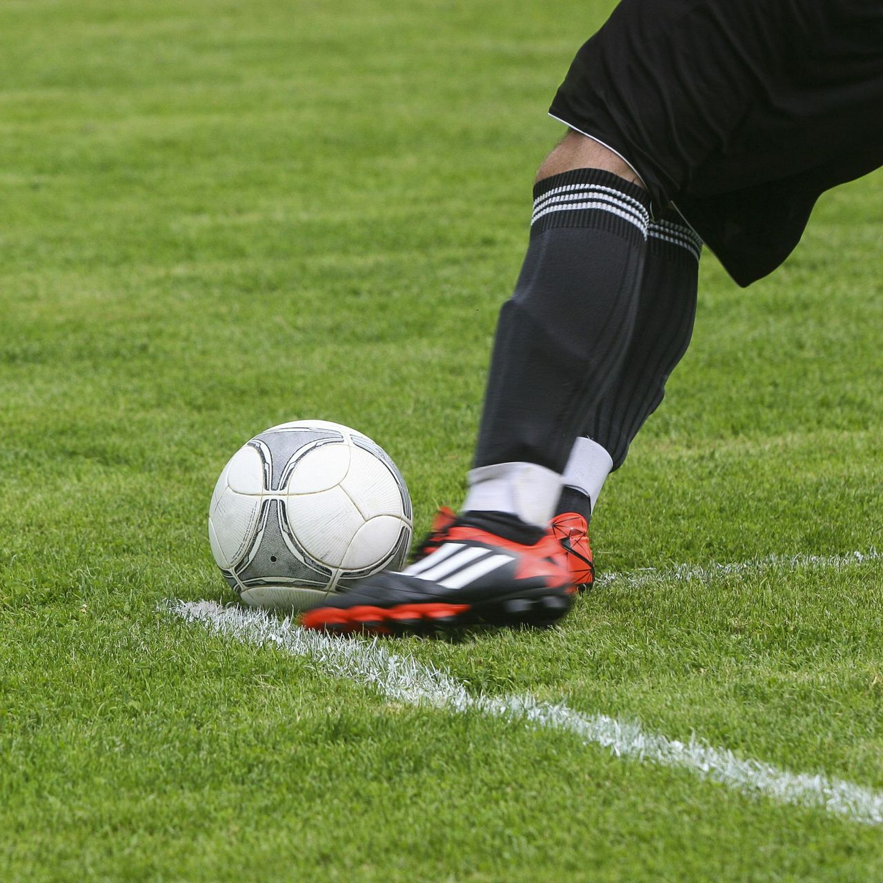 Soccer player kicking ball on a green field, close-up of foot, ball near white line.