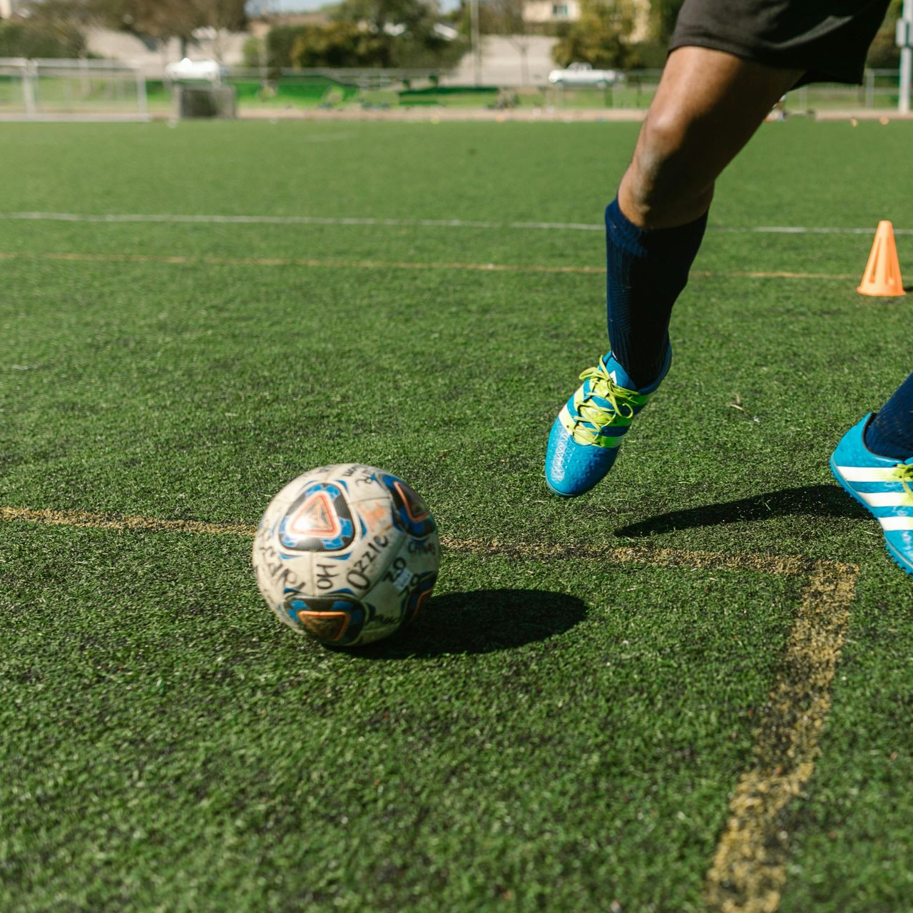 Soccer player kicking ball on green field, blue shoes.