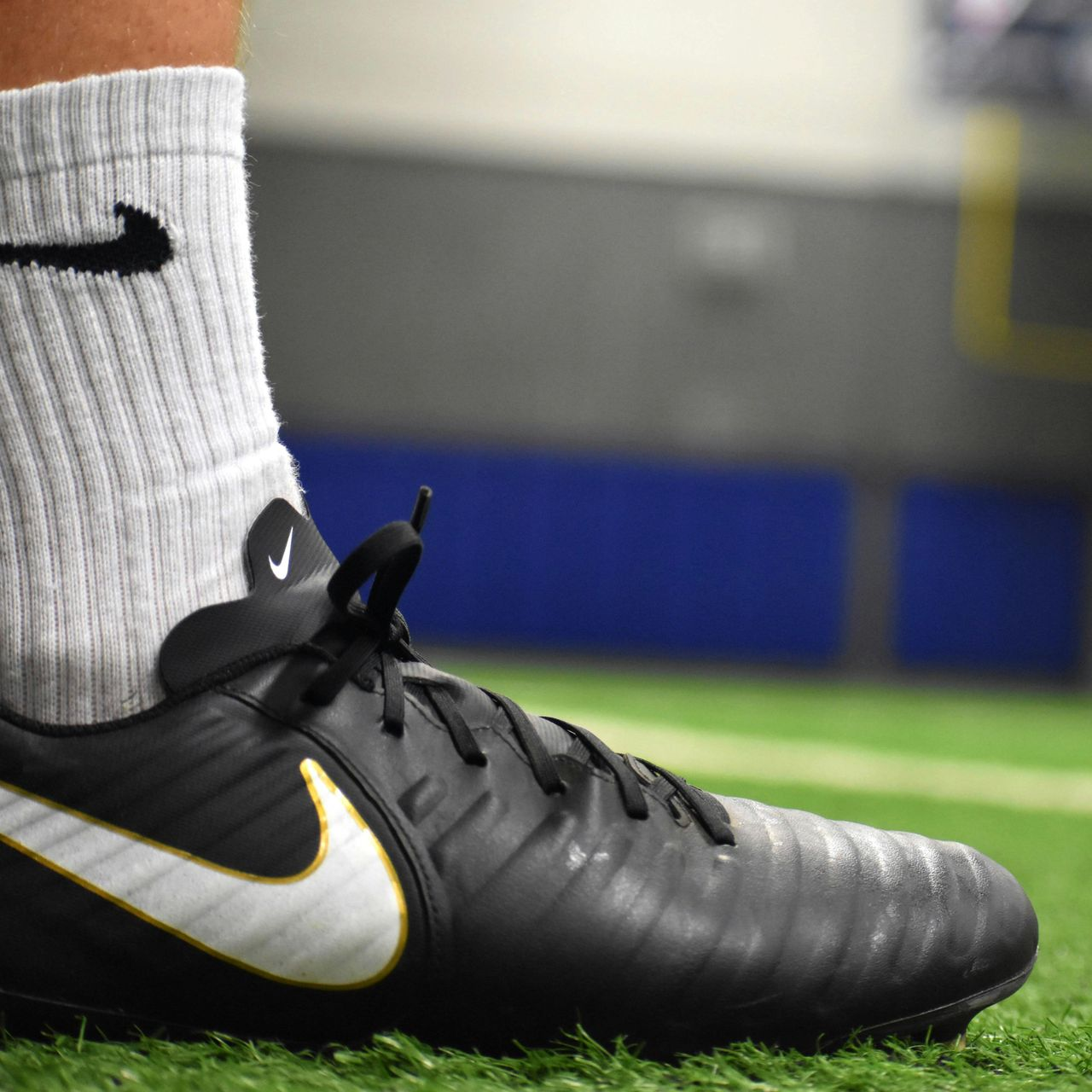 Black Nike soccer cleat on green turf, foot in white sock with black Nike logo.