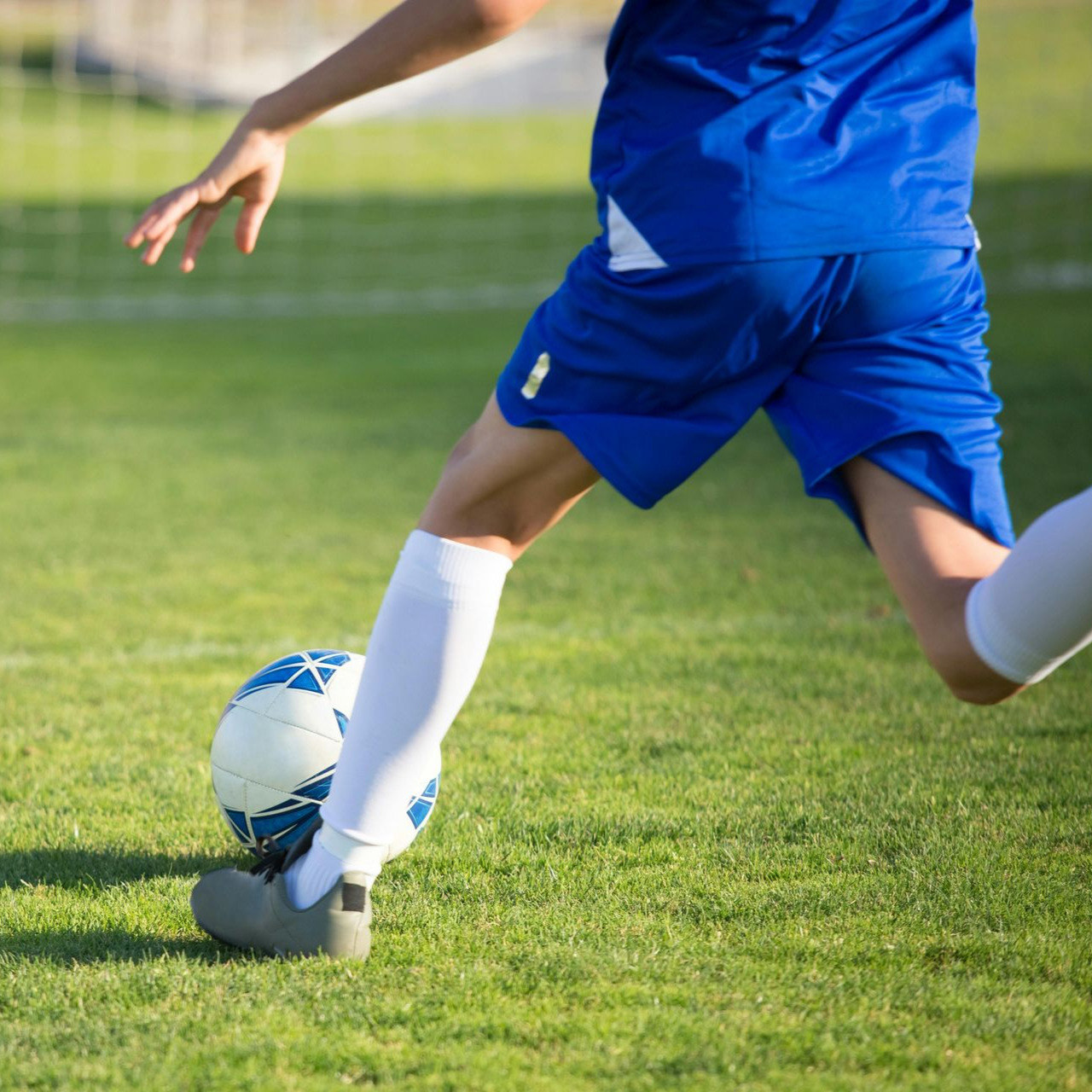 Soccer player in blue uniform kicking a soccer ball on a green field.