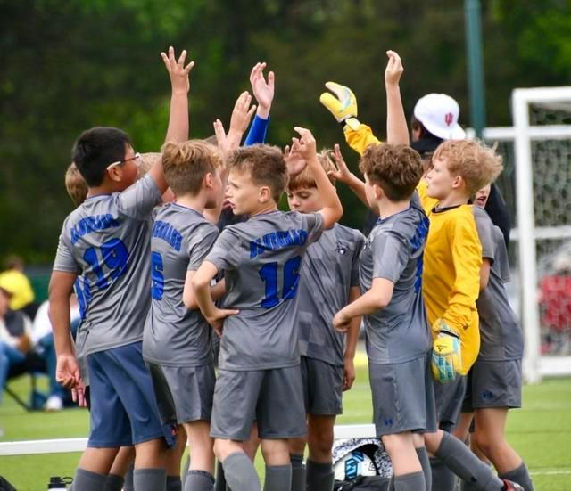 Youth soccer team in gray jerseys celebrating a win, arms raised on the field.