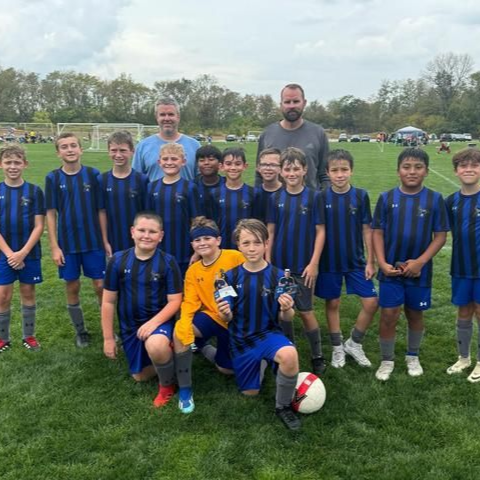 Youth soccer team posing on a field; blue uniforms, two adults, green grass, cloudy sky.