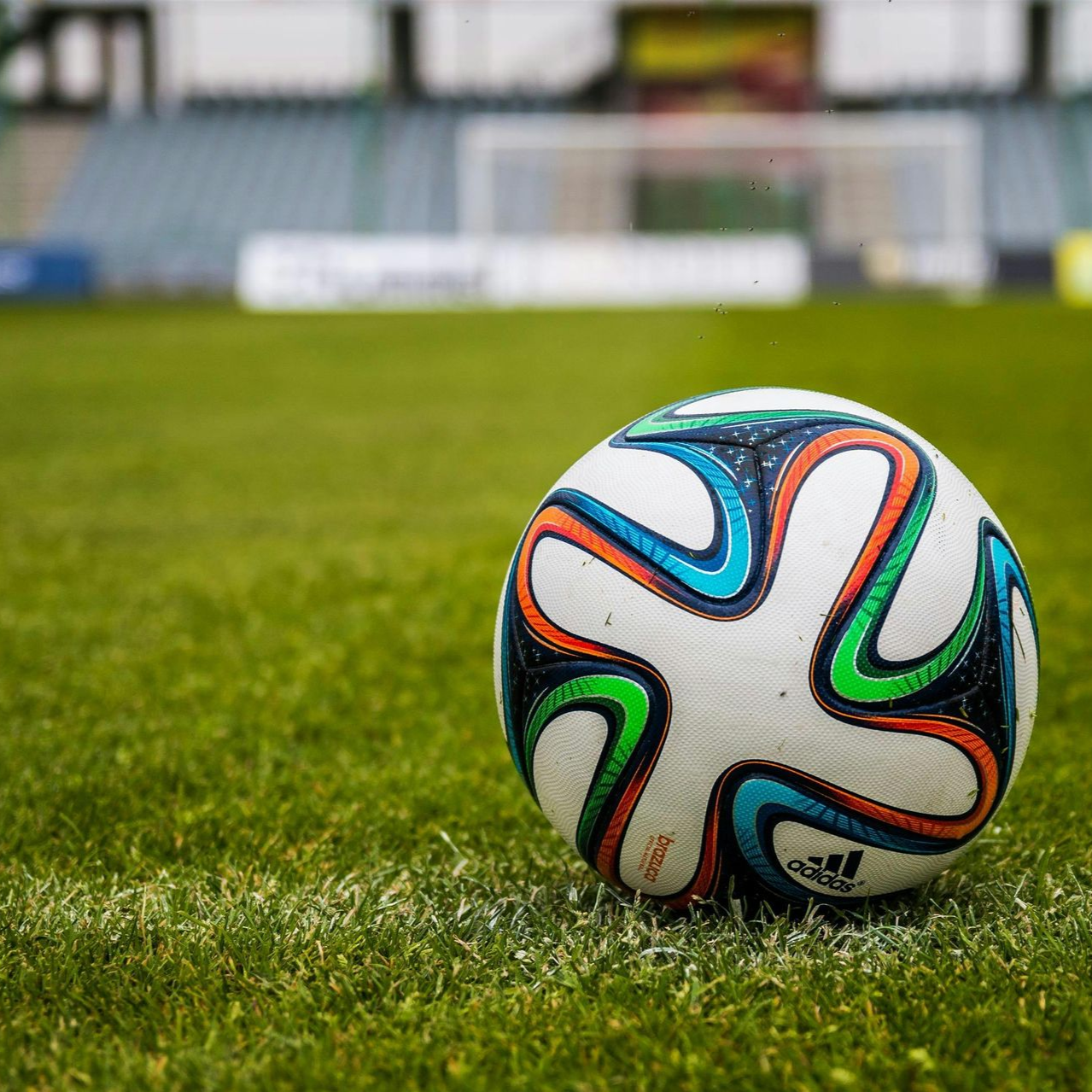 Soccer ball on a green field with a blurred stadium in the background.
