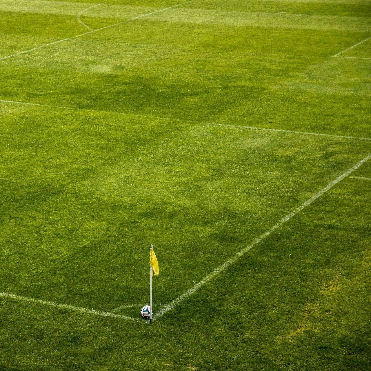 Soccer field corner with a yellow flag and a white ball.