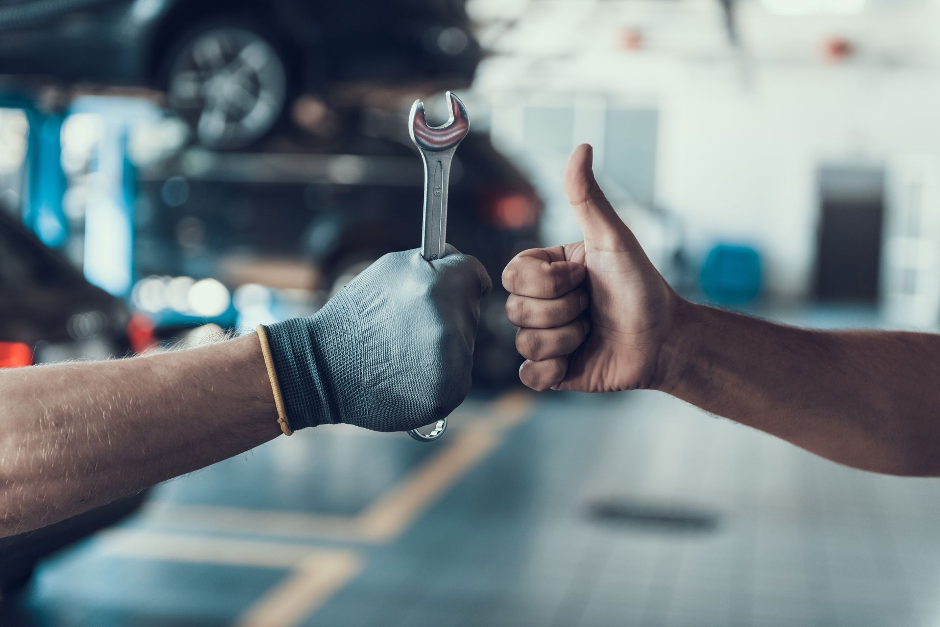Two men are holding a wrench and giving a thumbs up in a garage.