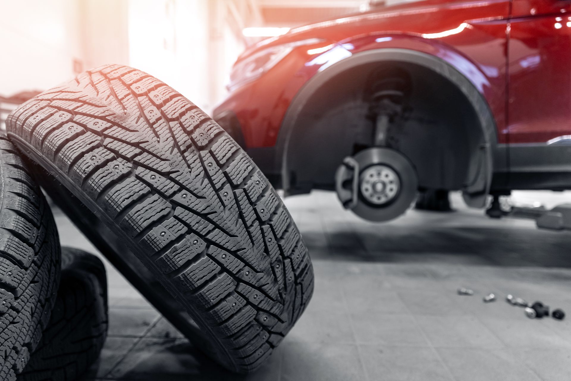 Deux pneus sont empilés l'un sur l'autre devant une voiture rouge.