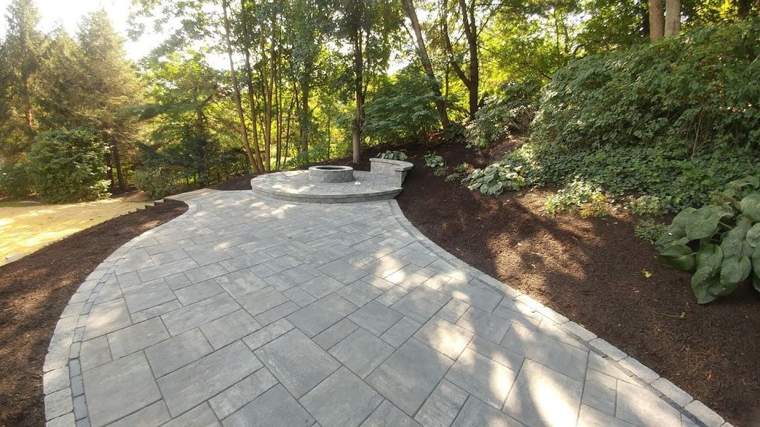 A brick walkway leading to a fire pit in the middle of a forest.