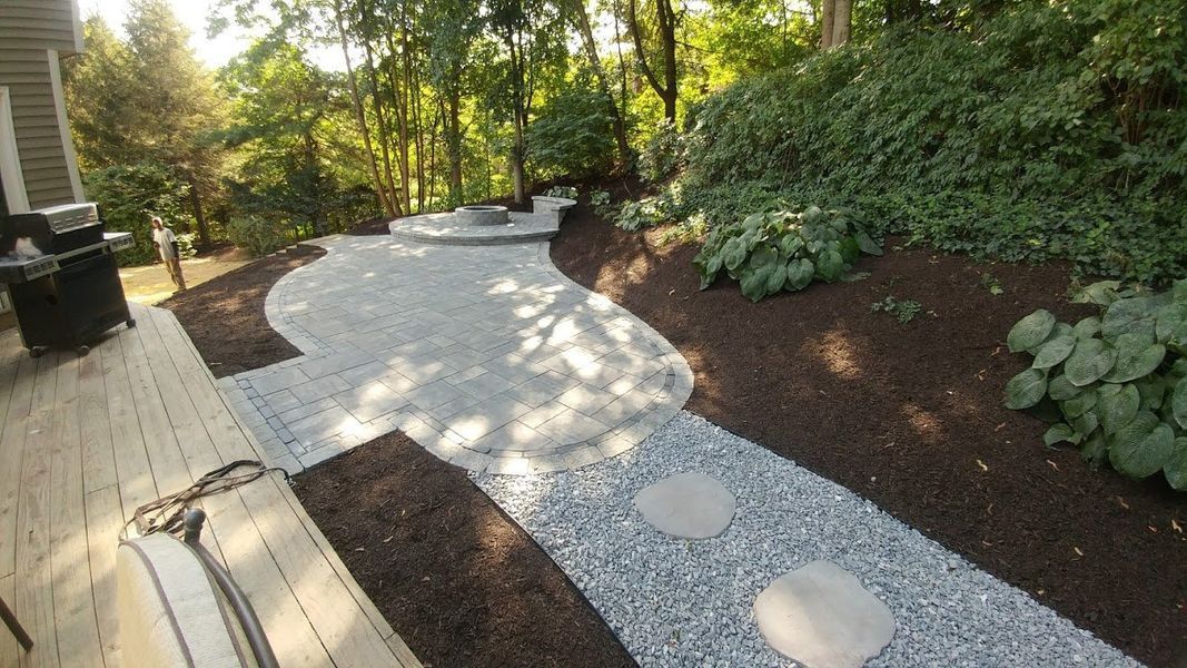 A stone walkway leading to a patio in a backyard surrounded by trees.