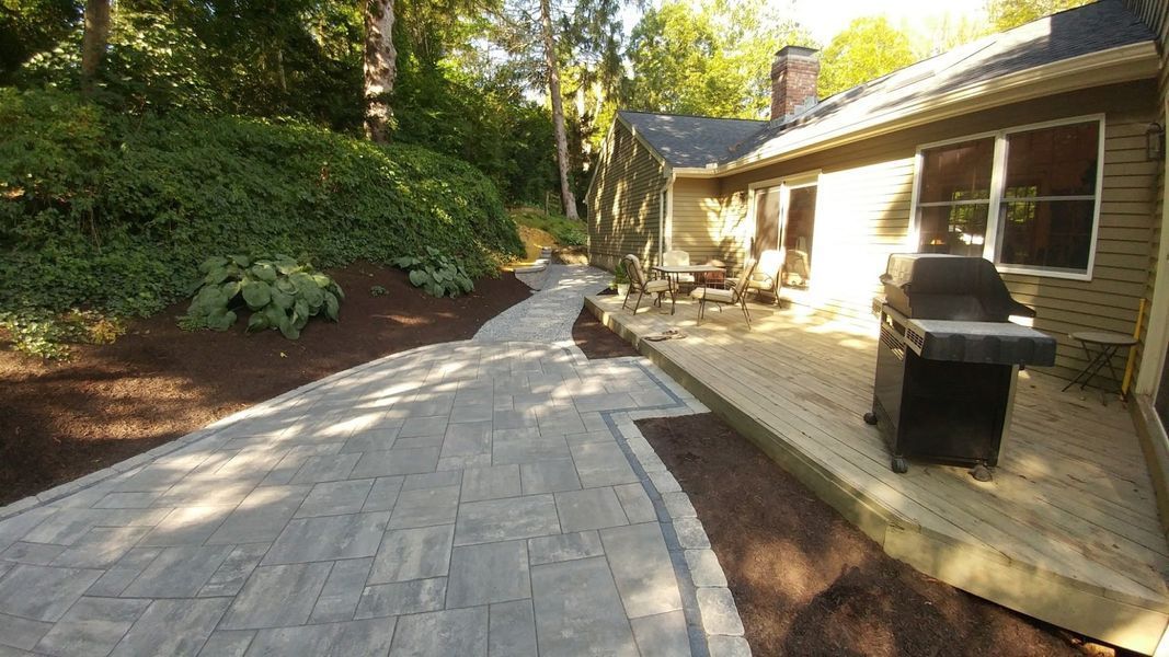 A patio with a grill and a walkway leading to a house.