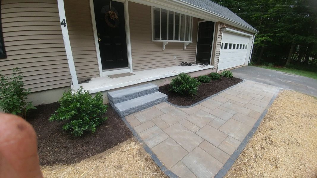 A person is standing in front of a house with a walkway and steps.
