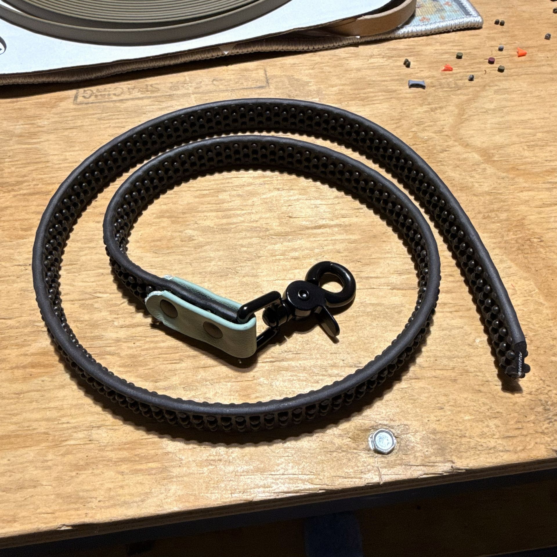 Five black studded straps with varying colored buckles and black carabiners on a wooden surface.