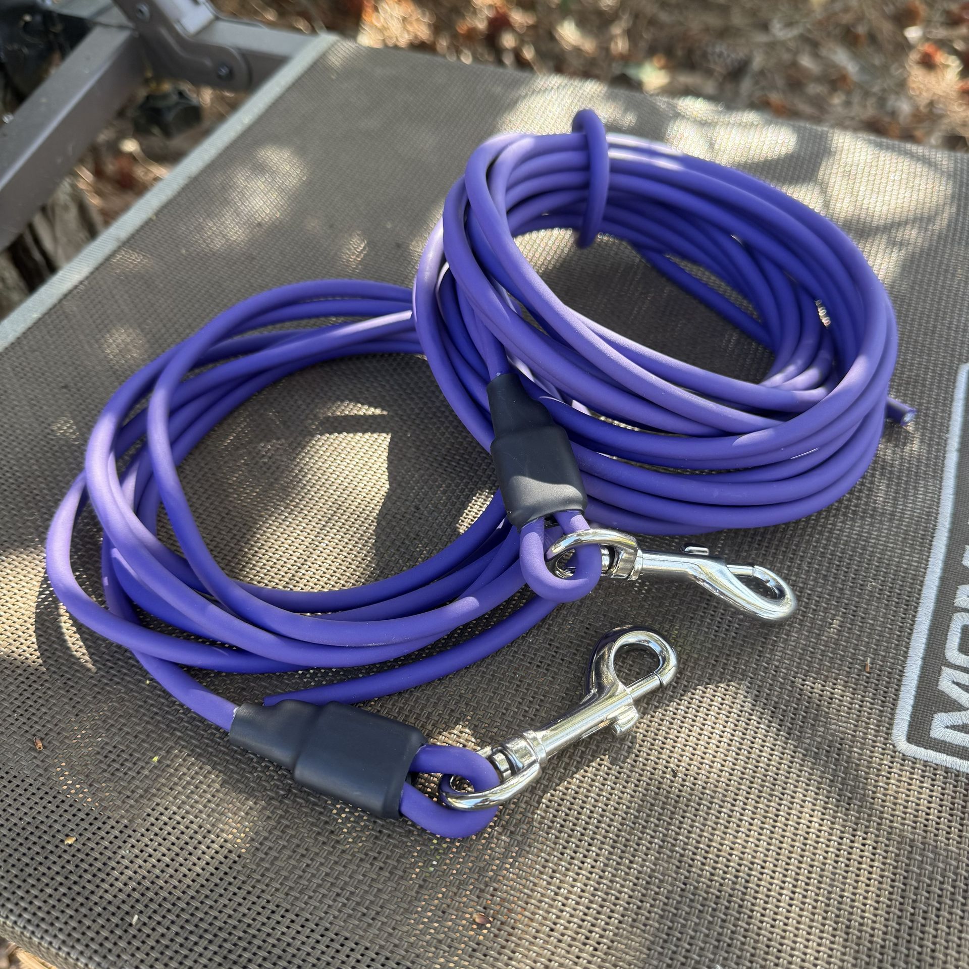 Two coiled bright orange leashes with silver metal clips, placed on a grey textured surface.
