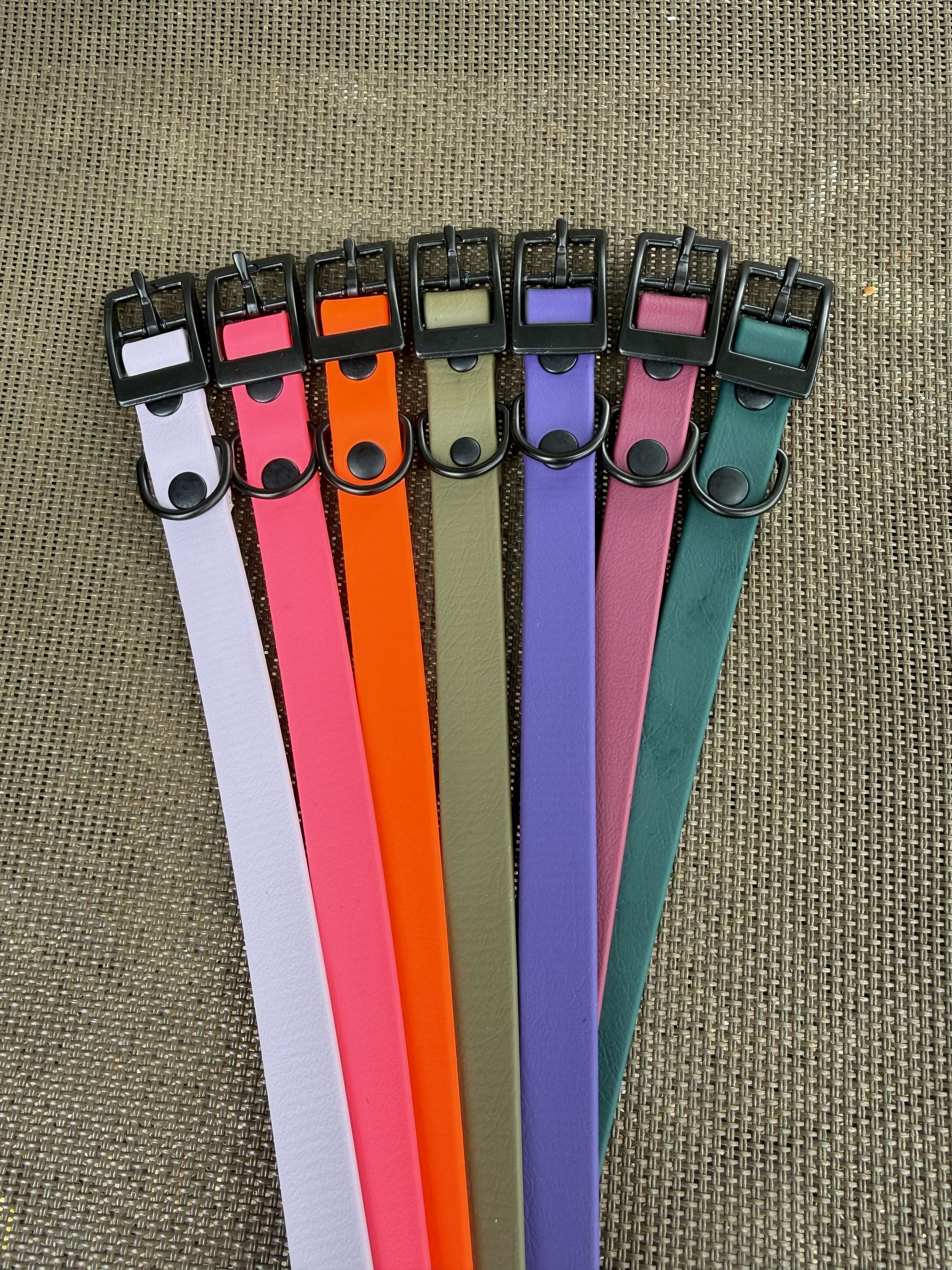 A vertical stack of brightly colored, flexible dog collars with black hardware, resting on a textured gray surface.