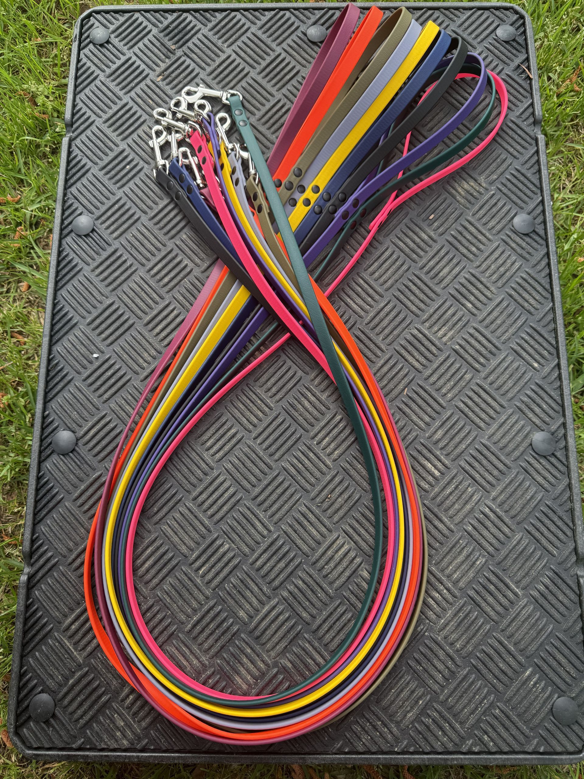 A bundle of colorful dog leashes with silver clips, fanned out and resting on a black, textured rubber mat outdoors.