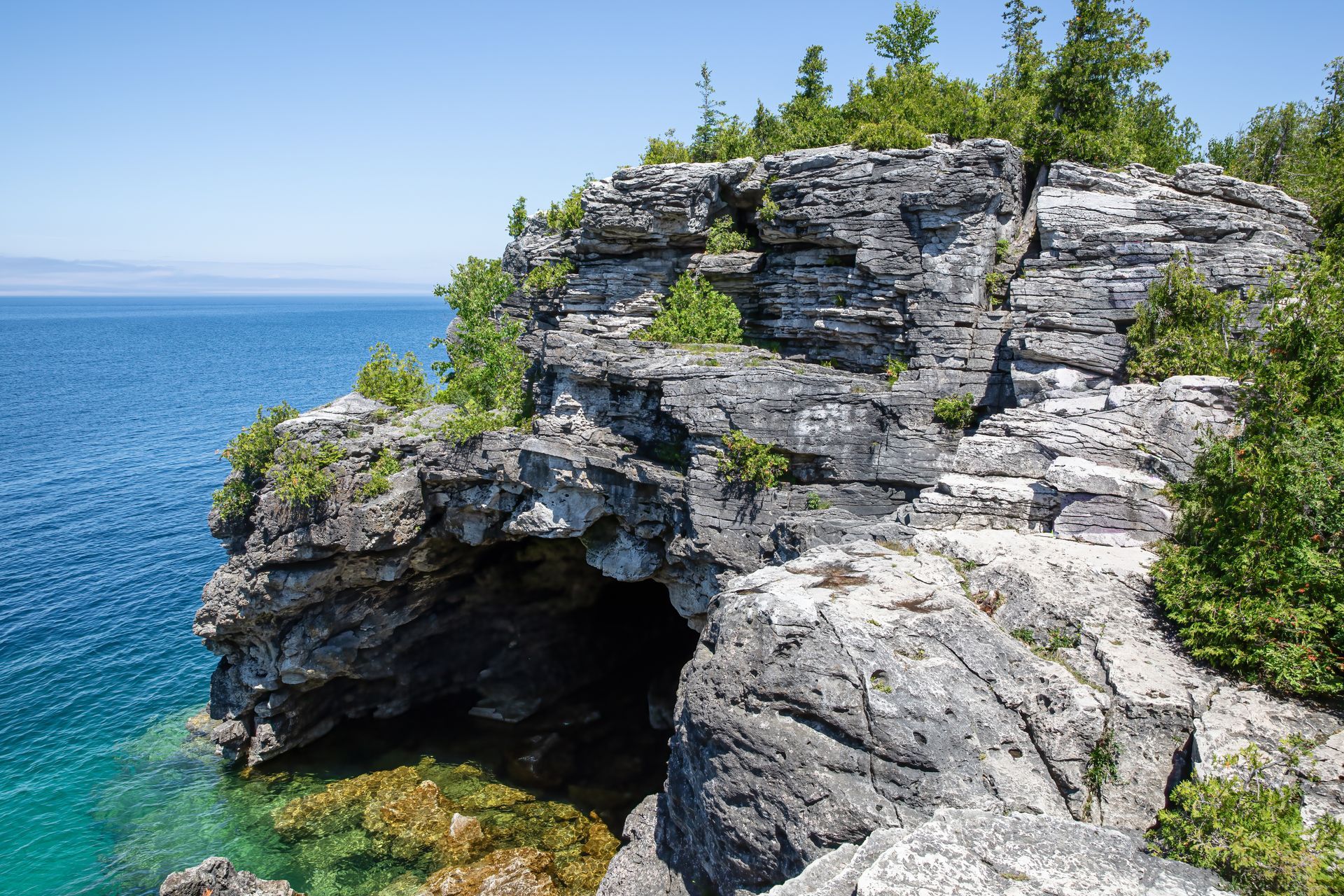 Rocky coastal cliff with a cave above turquoise blue water and green trees on top