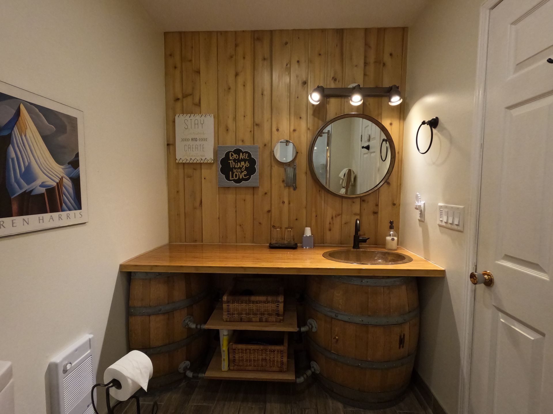 Small rustic bathroom vanity with wood paneling, round mirror, wall lights, baskets, and barrel-style sink cabinet