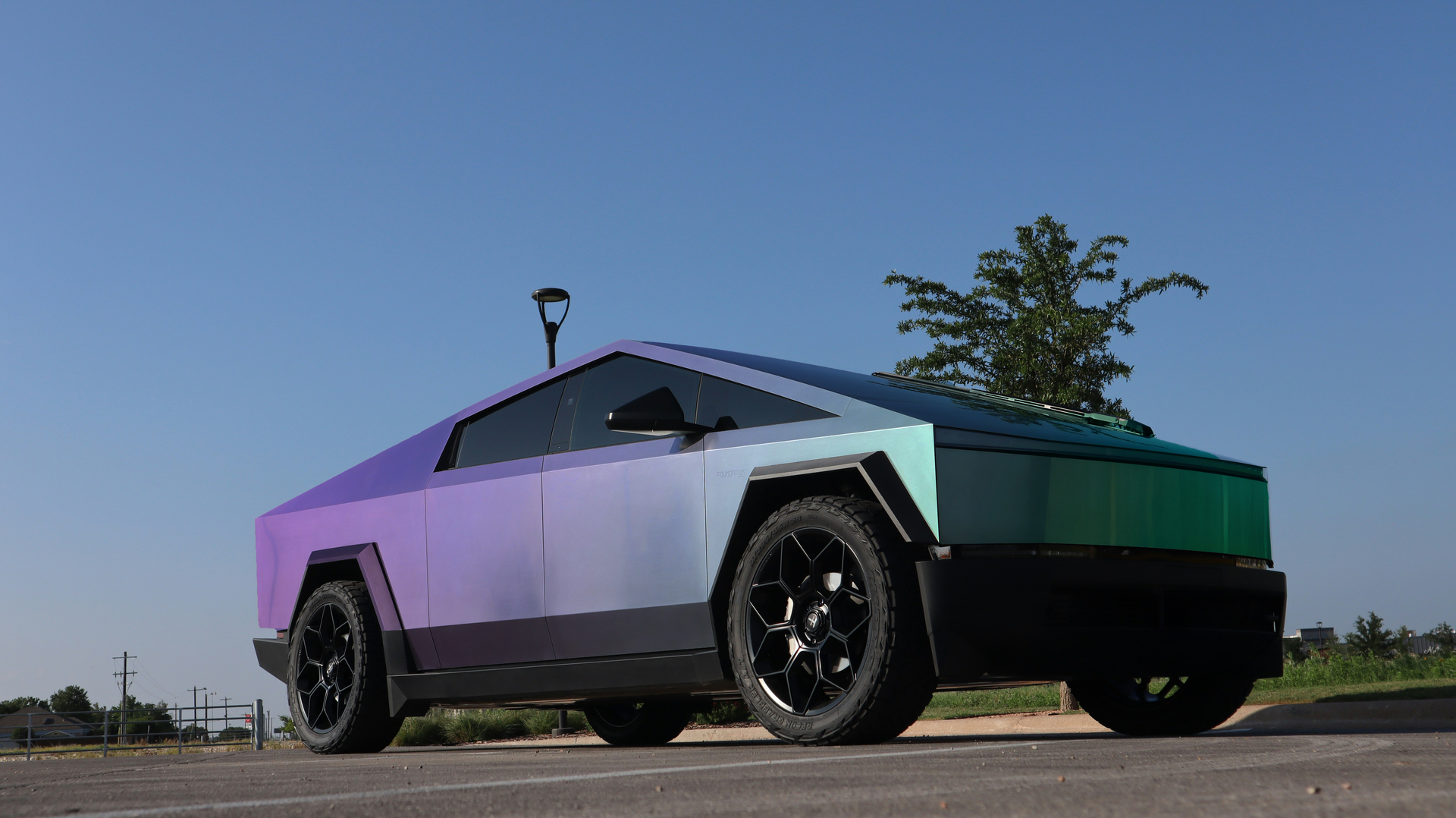 A purple and green tesla cybertruck is parked in a parking lot.