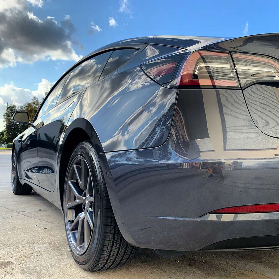 A black tesla model 3 is parked on the side of the road.