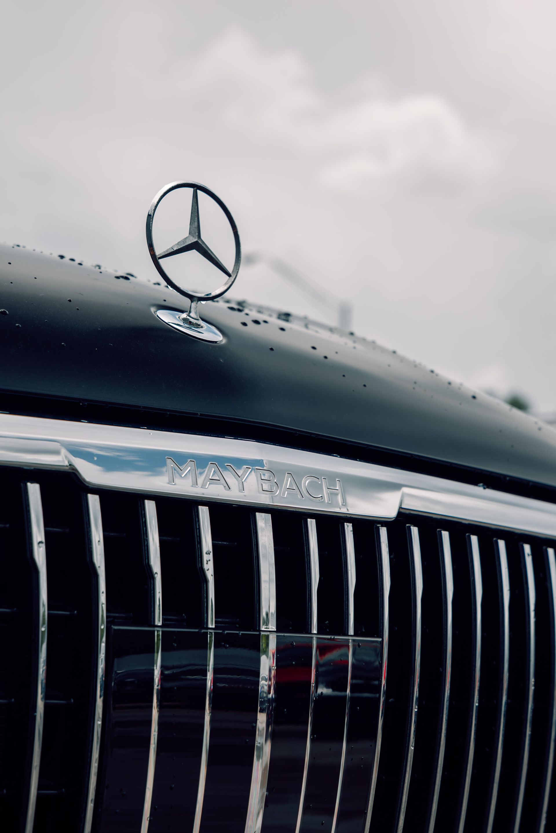 Close-up of a black Mercedes-Maybach hood with the brand's logo and chrome grill against a cloudy sky.