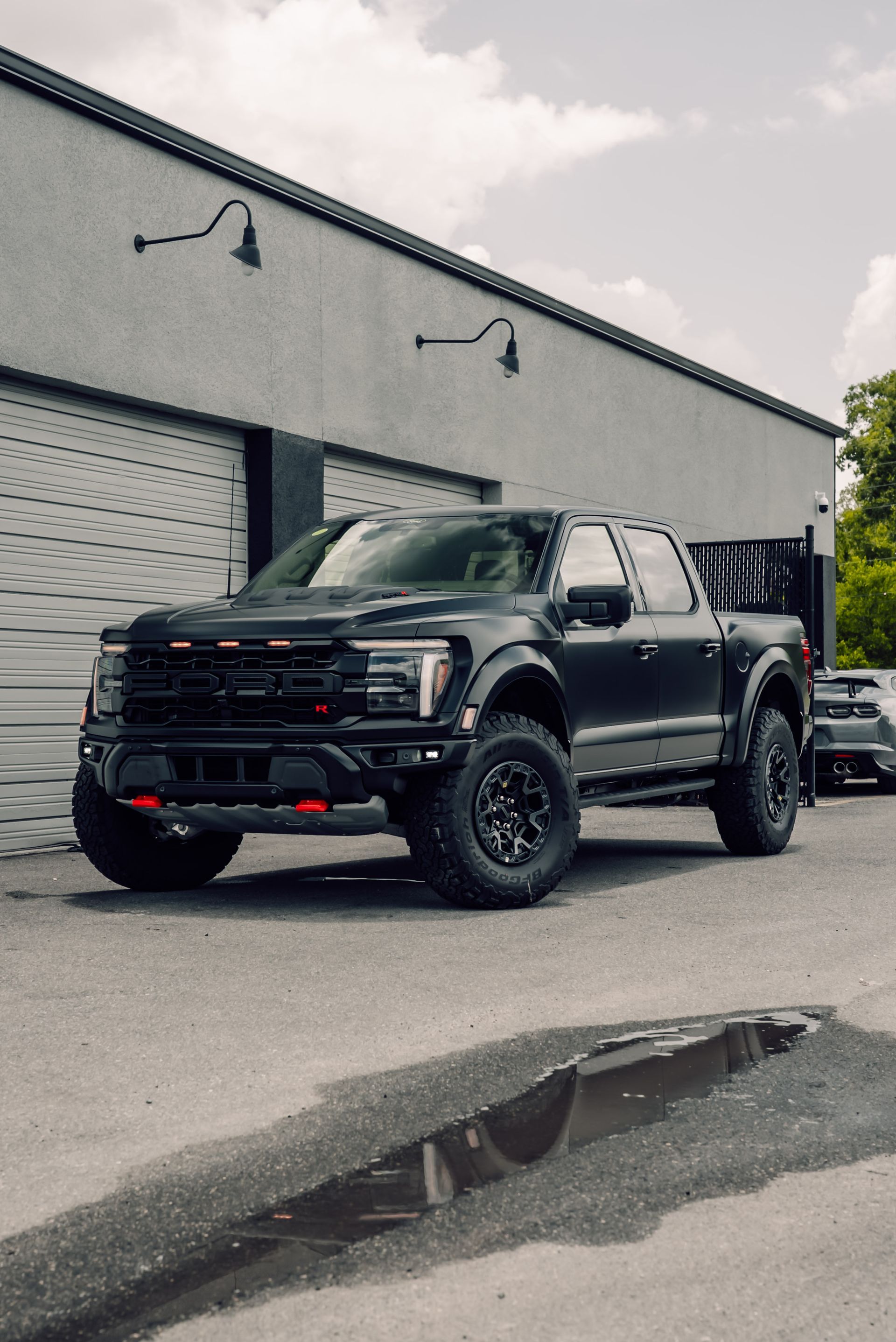 Black Ford F-150 Raptor truck parked outside a gray building.