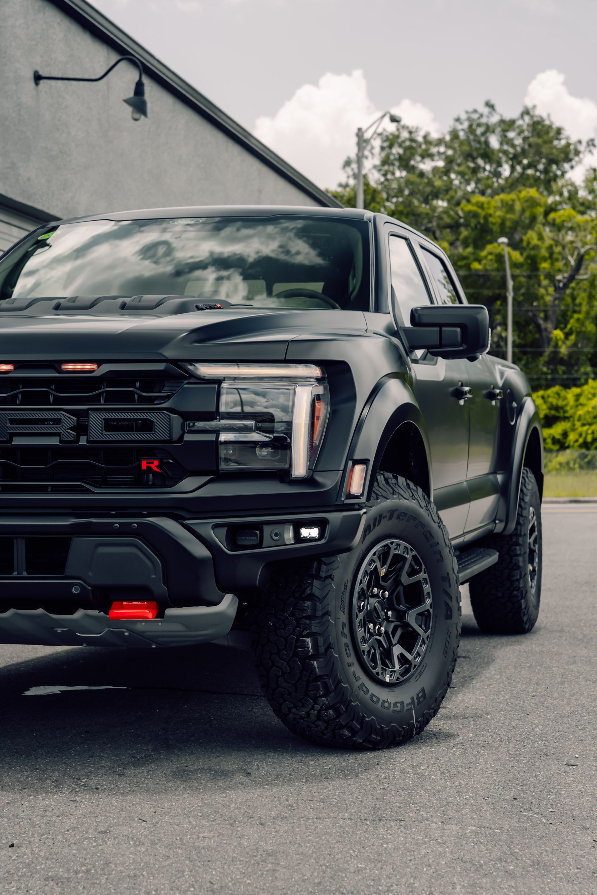 Black Ford F-150 Raptor truck parked on pavement in front of a building.