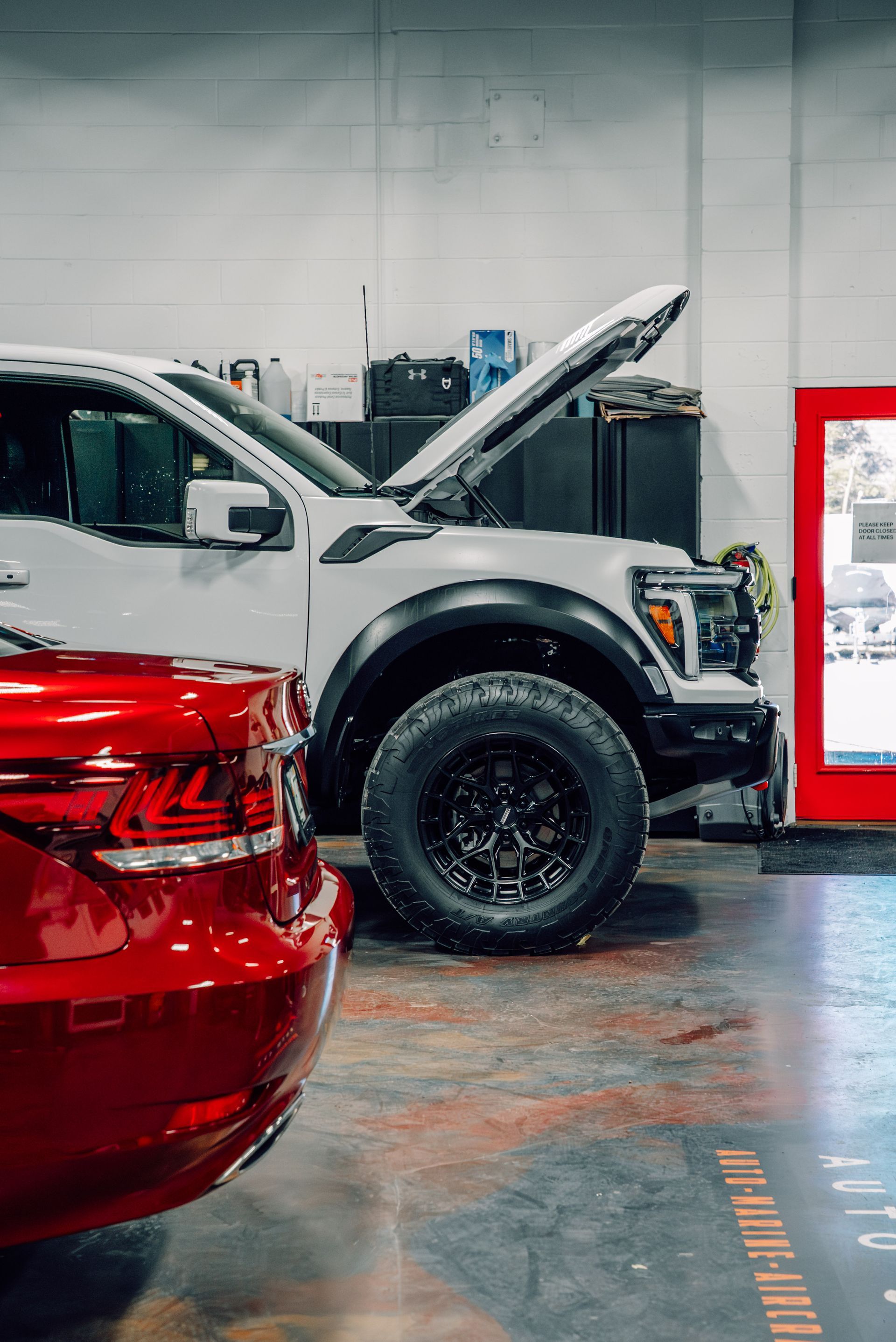 Red car and white truck with open hood inside a garage.