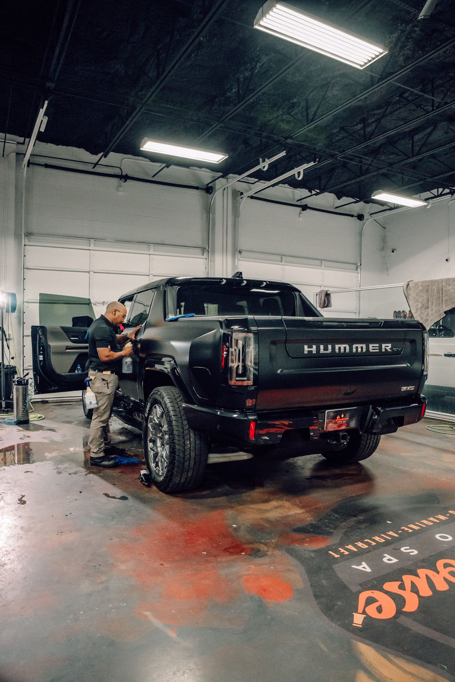 A mechanic working on a black Hummer pickup truck inside a garage.
