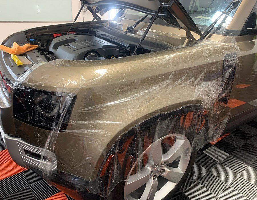 A car with its hood up is wrapped in plastic.