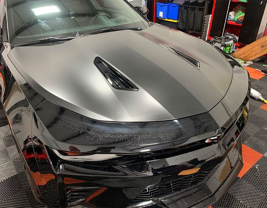 A black car with a hood scoop is parked in a garage.