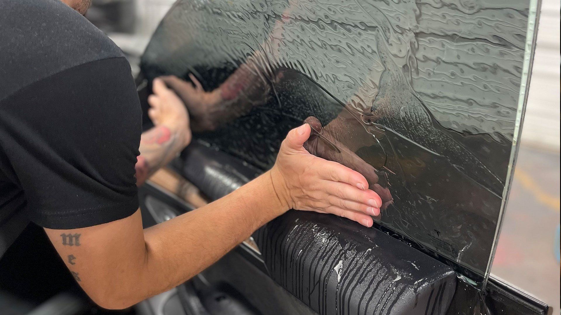 A person is applying tinted window film to a car window.